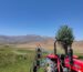 Red tractor in a vast agricultural landscape under clear blue skies with mountains in the background.